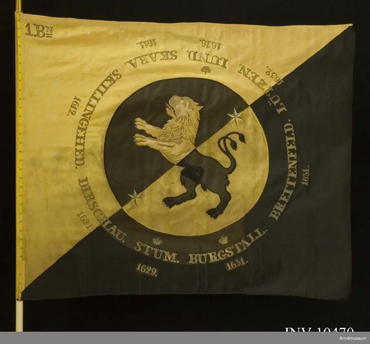 Duk av fansiden i fyrskaftad kypert, delad diagonalt i två fält - det inre gult och det yttra svart. I mitten en cirkel med 800 mm radie med omvända färger och där inne Västergötlands sköldemärke: ett lejon, gult på det svarta och svart på det gula fältet. I fältens delning finns två sex-uddiga stjärnor i guld. Lejonets svarta är applicerat fansiden  med kantsöm i svart silke, det gula är dels applicerat fansiden, dels schattérsöm i gult och vitt siden. Tungan fodrad i rött silke. Omkring vapnet, genombroderat i guld, finns segernamn: SKARA med "1611" under, SKILLINGEHED med 1612, DIRSCHAU och1627,  krönt STUM och 1629, krönt BURGSTALL och 1631, BREITENFELD och  1631, LÜTZEN och 1632 samt krönt LUND med 1676. I övre inre hörnet finns "1.Bn" broderat i guld (två streck  under N). Duken är kantad med ripsband, svart på det svarta och gult på  det gula. Fastspikad med förgyllda spikar. Kravatt av gult och svart kypertvävt fansiden. Guldfrans på kortändarna.

Hel längd 2860 mm, frans 10 mm, bredd 260 mm. Stång av furu - vitmålad. Doppsko konisk med rund knopp av förgylld mässing. Längd 2560 mm. Spets av förgylld mässing, ursprungligen med Oscar I:s krönta monogram som senare felaktigt byttes mot Gustav V:s krönta spegelmonogram inom lyra av lager. Längd 330 mm. Fodral av mörkblått (svart) kläde med skinnskodd topp, dragsko och ficka för spetsblad. Längd 1820 mm, bredd 180 mm.