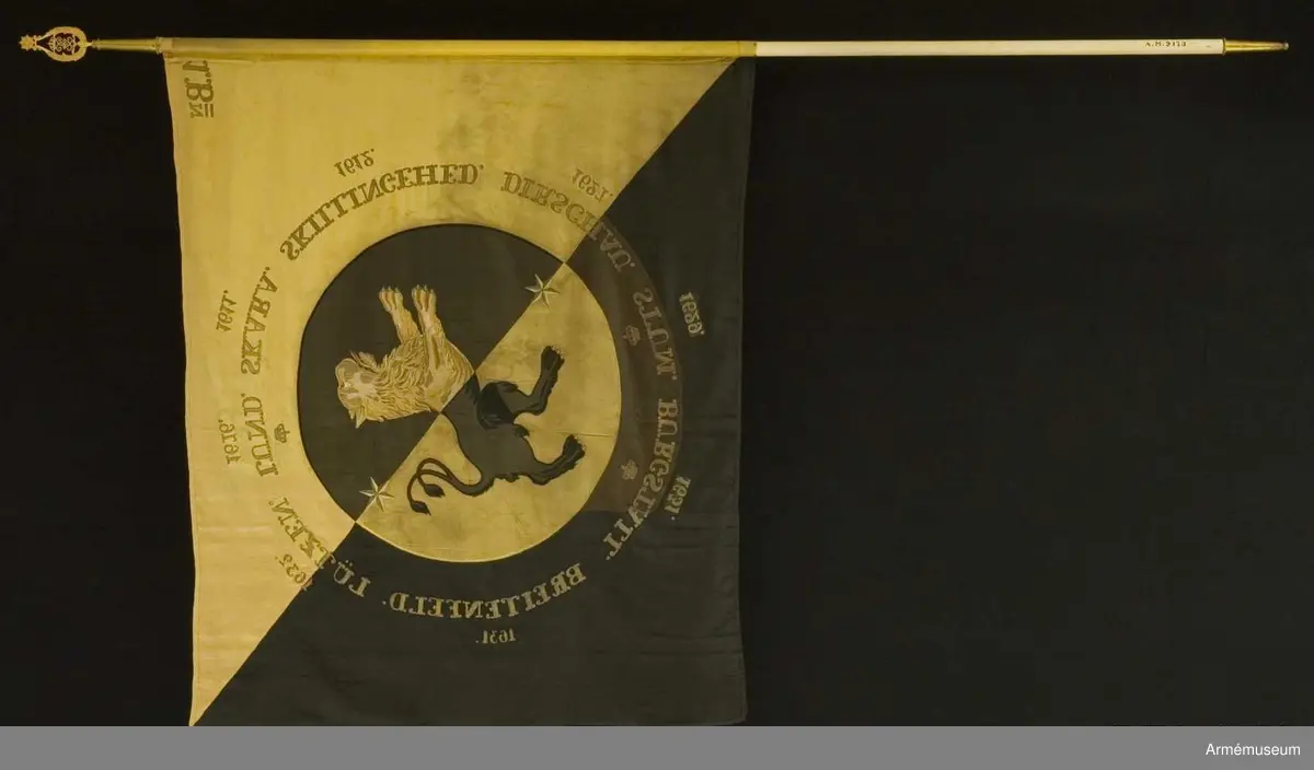 Duk av fansiden i fyrskaftad kypert, delad diagonalt i två fält - det inre gult och det yttra svart. I mitten en cirkel med 800 mm radie med omvända färger och där inne Västergötlands sköldemärke: ett lejon, gult på det svarta och svart på det gula fältet. I fältens delning finns två sex-uddiga stjärnor i guld. Lejonets svarta är applicerat fansiden  med kantsöm i svart silke, det gula är dels applicerat fansiden, dels schattérsöm i gult och vitt siden. Tungan fodrad i rött silke. Omkring vapnet, genombroderat i guld, finns segernamn: SKARA med "1611" under, SKILLINGEHED med 1612, DIRSCHAU och1627,  krönt STUM och 1629, krönt BURGSTALL och 1631, BREITENFELD och  1631, LÜTZEN och 1632 samt krönt LUND med 1676. I övre inre hörnet finns "1.Bn" broderat i guld (två streck  under N). Duken är kantad med ripsband, svart på det svarta och gult på  det gula. Fastspikad med förgyllda spikar. Kravatt av gult och svart kypertvävt fansiden. Guldfrans på kortändarna.

Hel längd 2860 mm, frans 10 mm, bredd 260 mm. Stång av furu - vitmålad. Doppsko konisk med rund knopp av förgylld mässing. Längd 2560 mm. Spets av förgylld mässing, ursprungligen med Oscar I:s krönta monogram som senare felaktigt byttes mot Gustav V:s krönta spegelmonogram inom lyra av lager. Längd 330 mm. Fodral av mörkblått (svart) kläde med skinnskodd topp, dragsko och ficka för spetsblad. Längd 1820 mm, bredd 180 mm.