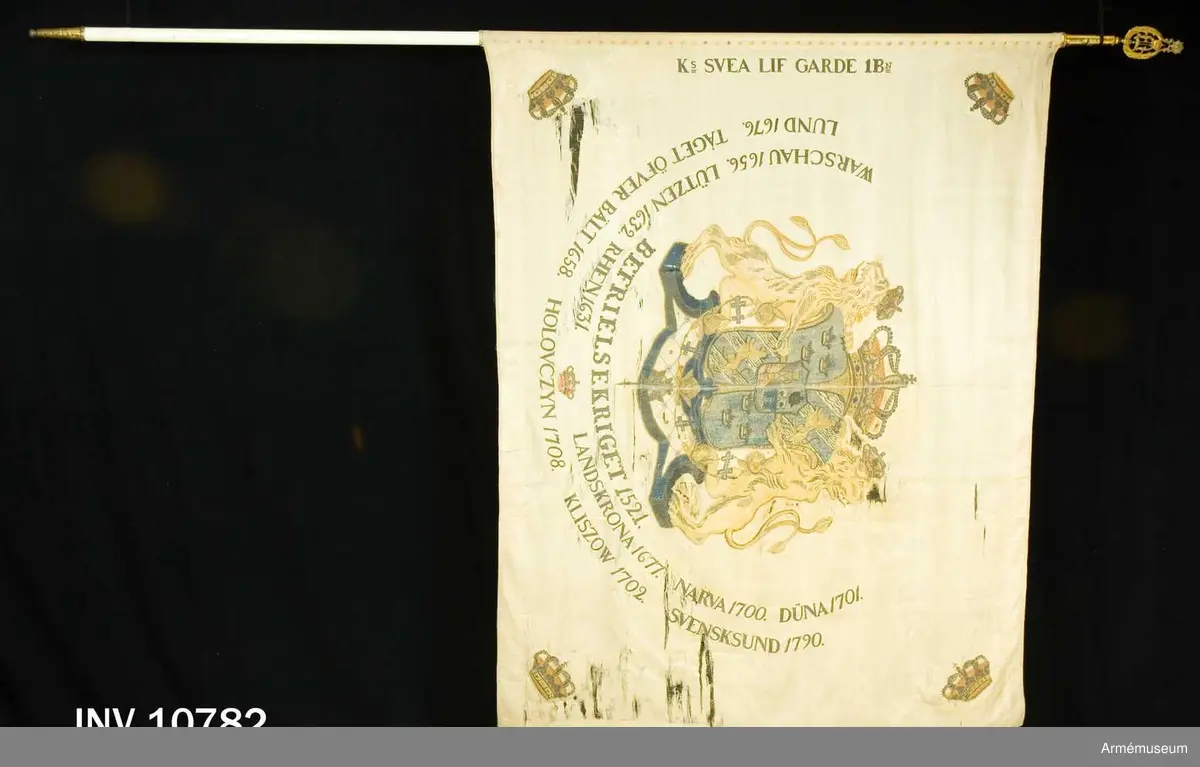 Duk av vit sidenkypert varå broderat lika å båda sidor, riksvapnet omgivet av segernamnen, slutna kronor i hörnen. Kravatt med guldfrans tillhör. Fanstången är vitmålad. Spets med Oskar II:s namnchiffer.