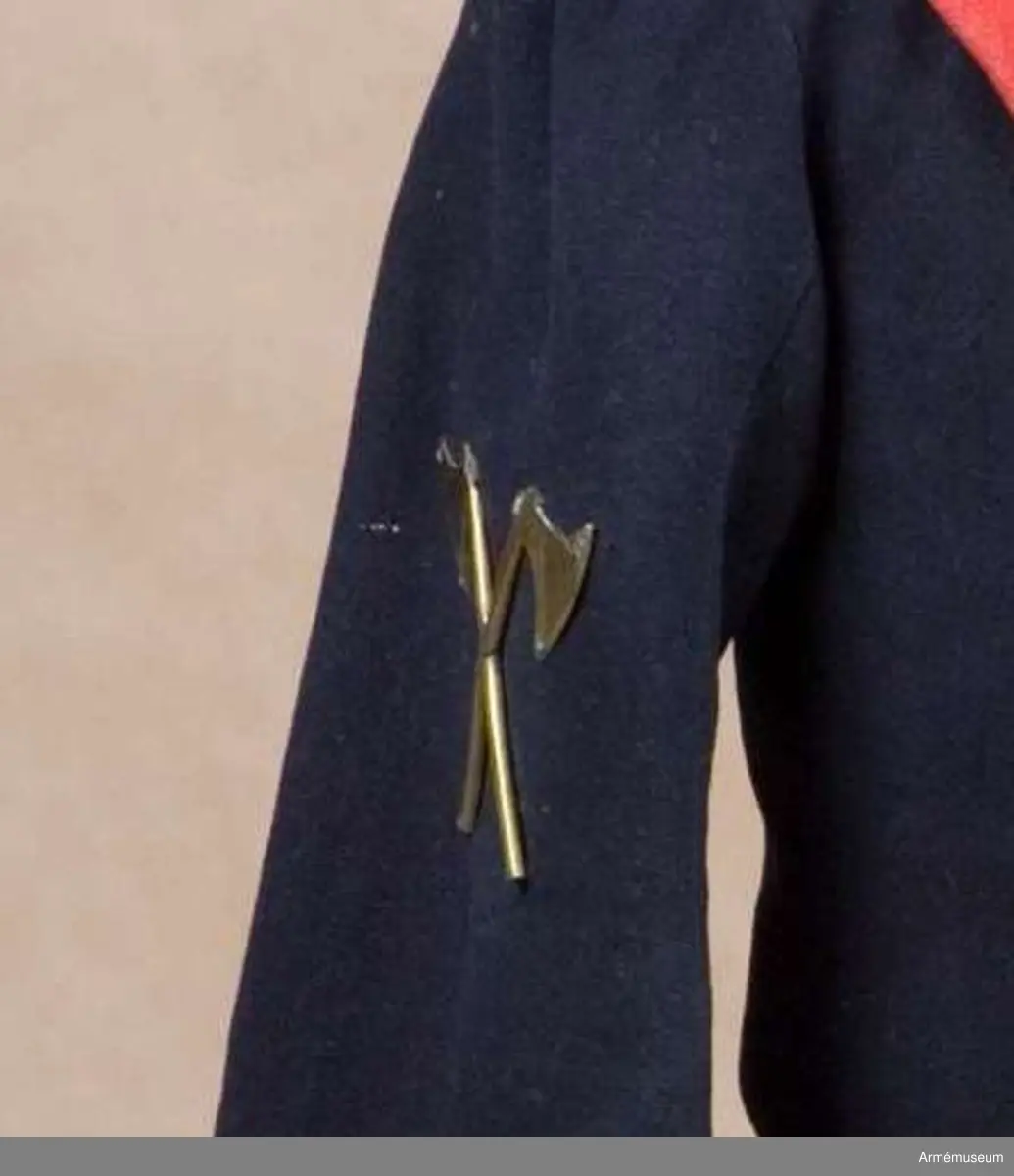 Två distinktionstecken av mässing i form av två korslagda yxor. Tecknen har 8 hål för fastsättning på uniformen.
Tecknen är fastsydda på fracken AM.015502:s ärmar.

Till distinktionstecknen hör en modelletikett med rött vaxsigill och följande text:
"Modell till Öfver-Timmermans distinction, att fästas på båda Jack ärmarne, Nådigast approberad under dena dag, Stockholms Slott d. 26 Aprill 1832, På nådigaste befallning M. Brahe, General Adjutant för Armén".
Sigillet pryds av Lilla Riksvapnet i mitten med följande text runt om: "Konungens Gen. Adjuts. Exprd. för Arméen".