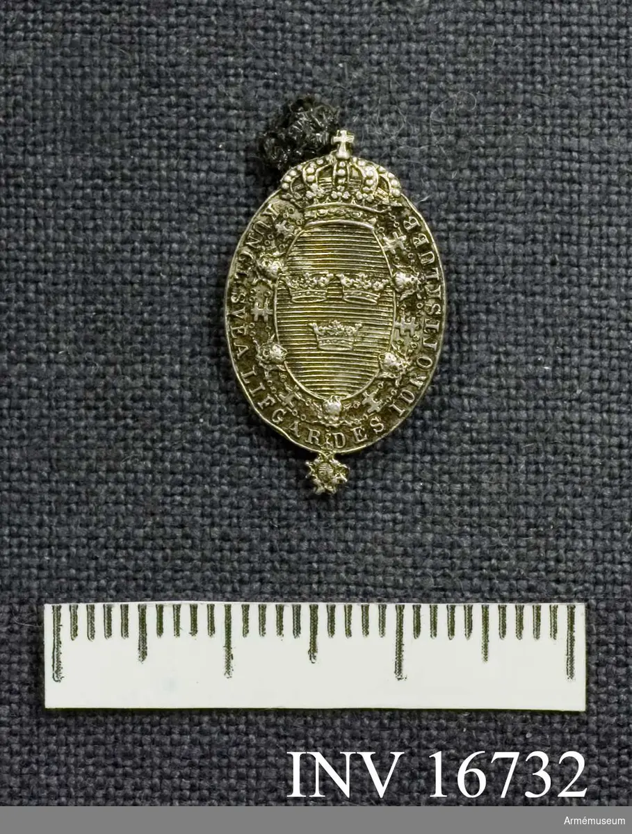 Ett ovalt nålmärke av silver. Visar riksvapnet.

Samhörande nr är AM.16715-32