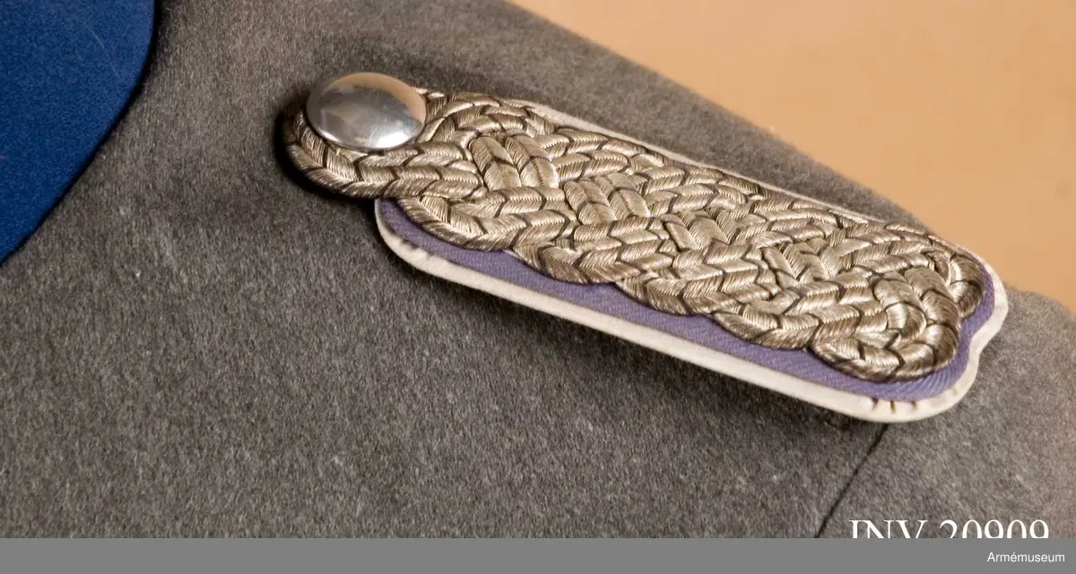 Av flätade tränsar i oxiderat silver med ljusblått tyg under tränsarna och med underlägg  av vitt bomullstyg (ljusblått och vitt är regementsfärger för Kyrassiärregementet nr 3). Axelklaffarna saknar stjärnor. Tränsarna utvisar stabsofficerare, stabsofficerare, majors grad. Under axelklaffarna finns ett  ett stycke vitt tyg (axelklaffstunga) med knapphål.