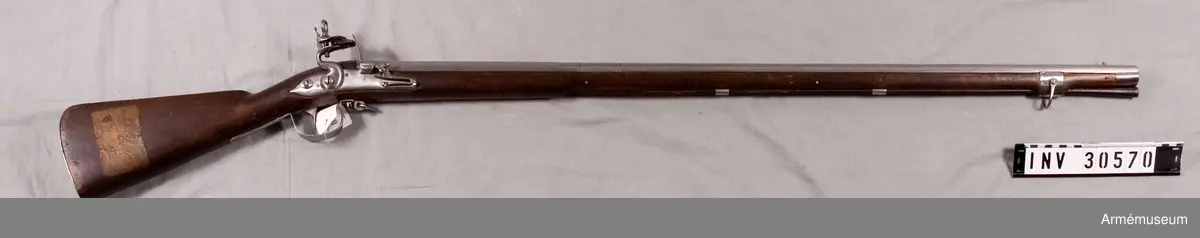 Grupp E II.

Nominalkaliber: 20,04 mm, verklig 20,3 mm.
Kammarstycket är 30,6 cm långt, baktill åttkantigt, längst fram på en längd av 2,7 cm åttkantigt, framtill begränsat av en upphöjd och två insvarvade ränder. Tre liknande ränder gå kring det runda långa fältet 4,7 cm framför kammarstyckets främre ände, och 0,3 cm framför de sistnämda ränderna gå åter tre dylika ränder kring pipan. Knappformigt korn 4,1 cm bakom mynningen. Lågt ståndsikte längst fram på svansskruvsstjärten. På kammarstyckets översida otydlig stämpel och en med bokstäverna P O, på vänstra sidan två monogramstämplar, en med H L och en med P S samt längre ned siffran 7, på undersidan I H. Tre häften, nedifrån isatt korsskruv.

Låset har kullrigt, baktill i spets utlöpande bleck, nit i stället för pannskruv, hanhalsen baktill plan, läppskruven avslutas av en ring med 2 cm yttre diam., eldstålsfjäderns skruv går utifrån och eldstålsfjäderns bukt går framför främre låsskruvens ände. Pannstjärten är kort. På låsbleckets utsida ett inslaget S. Låset fasthålles av två skruvar. Säkringen består av en på låsets insida liggande regel, på vilken en på dess inre sida liggande, av stångfjäderns skruv fasthållen bladfjäder trycker. Regeln har ungefär på mitten en kort klack och fjädern gör vid änden en bukt. Regeln manövreras genom en på låsbleckets utsida nära bakspetsen liggande knapp, som på insidan har en arm, vilken går genom ett spår i låsblecket och vilken genom en nit fasthålles vid regeln. När låset ej är säkrat, ligger den nyss omtalade bladfjäderns bukt framför regelns klack. Vill man säkra låset sätter man det i halvspänn, skjuter den på bleckets utsida liggande knappen framåt, varvid regelns främre ände infaller i ett hak på nöten och sålunda spärrar låset. Då regeln går  framåt, trycker dess klack undan fjäderns bukt, vilken, då regeln kommit så långt fram som den kan, lägger sig bakom regelklacken och sålunda håller regeln stilla.

Björkstock, ursprungligen svartbetsad. Plan kolvrygg, avrundad häl, kräva. Baktill på kolvens högra sida inslaget 7 och 2. Järnplåtsbeslag, bestående av bakplåt, som fasthålles av stift, stor varbygel, vars bakre arm fasthålles av två stift, och vars främre, som längst fram är utbildad till en ögla, fasthålles av korsskruven, kort avtryckarebleck, som fasthålles av två stift, kraftigt S-formigt, i jämnhöjd med stockens yta infällt platt sidbleck, två släta mellanrörkor, 3,15 cm brett näsbleck. Den bakre rembygeln är fäst i varbygelns ögla, men den U-formade främre skruv, som går genom krävbeslaget och genom främsta häftet. På bakåplåten är siffran 7 inslagen. 

Laddstocken är av trä och har på smaländen ett 5,1 cm långt, med gängat hål för kratsen försett järnbeslag. Till vapnet hör en krats, som dock utställes särskilt under nummer AM 6350.

På en vid kolvens högra sida fastklistrad lapp står "Project till Infanteri Mousqvet Åhr 1687". Årtalet har senare genom påritning gjorts tydligare. Låset är tillverkat av bössmeden Pieter Starbus i Stockholm. I modellsalens reversal återfinnes musköten bland "Musköter och infanterigevär, svenske, med flintlås, 1689 års". I 1813 års inventarium över modellkammaren vid Kongl. Beväringsförrådet är vapnet upptaget bland "Modeller, projecterade" som "Mousquette, 1689 års". I Artillerimuseum har vapnet från 1879 alltid kallats "Infanterigevär med flintlås, projekt 1687" med varierande ordalydelse. J. Alm 1937. Kulvikt 36,6 g. Loppets rel. längd 34 kal. Flintlås.
