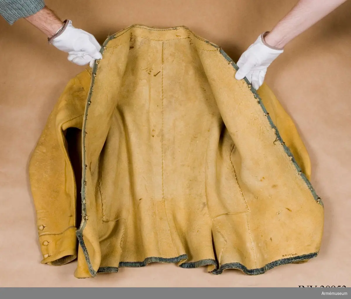 Kyller av gul älghud med smala blå linneband som kantning på insidan samt som passpoal vid övre kant av ärmuppslagen.
Helt framstycke med utsvängt kort skört med uppvik framtill, samt bakstycke med mitt-bak-söm och två sidstycken. Sidsöm under ärmen. Formad tvåsömsärm med ärmuppslag. Ärmuppslagen har sprund som knäpps med 3 koniska älghudsknappar i varje sida, även om det är utskuret 6 knapphål i höger ärm och 5 i den vänstra. De knapphål som inte används är ihopsydda. Liten axelkarm, samt axelklaffar på båda sidor som är fastsydda vid axelsömmen samt knäpps med älghudsknapp vid halsen. Knapp saknas på vänster axel.
Låg ståndkrage som har varit kantad på insidan med blått band. Detta saknas i dag.
Plagget knäpps kant i kant med 12 stycken hyskor och hakar mitt fram. Alla sömmar är sydda med oblekt lintråd.
Märkt inuti ryggen "No 1".
Kyllret skiljer sig något från samtida kyller av samma modell genom att de blå banden är smalare.