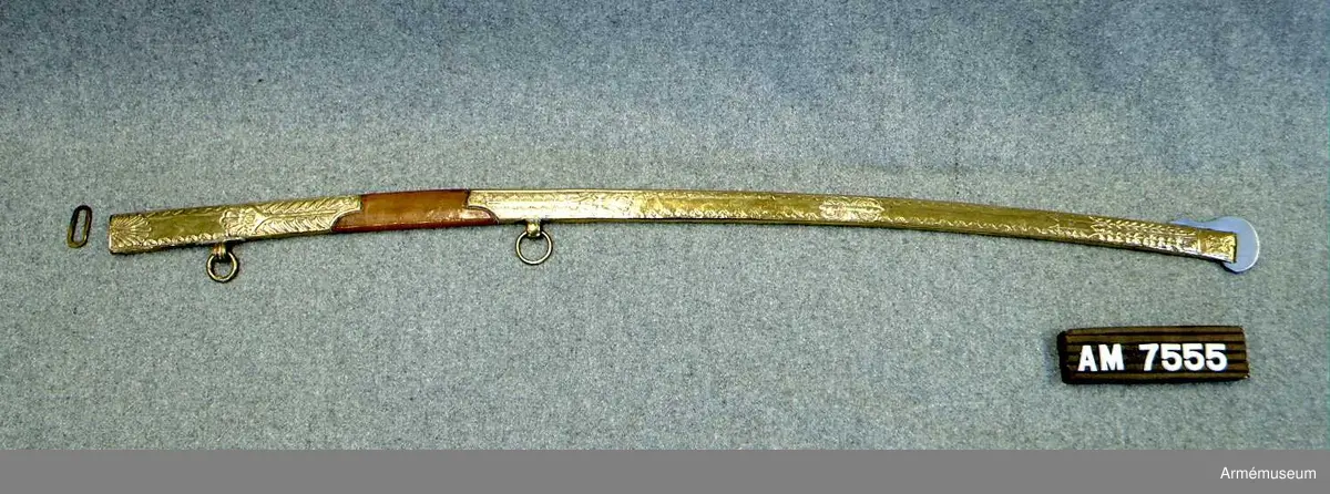 Balja med beslag av förgylld mässing, mittparti läderklätt. Släpsko av stål. Baljan är av brunt läder och har munbleck och mycket lång släpsko av förgylld mässing, som är driven i stiliserade blomornament m.m. 
Släpskon är längst ned på änden och vid framsidan skodd med stål. 
Munbleckets nedre och släpskons övre kant är enkelt fasonerad. 
På ryggsidan har munblecket och släpskon var sin ögla för en koppelring. 
Dessa öglor har längs kanterna förhöjda ränder och pryds på mitten av fina prickar. 
Koppelringen är av mässing.