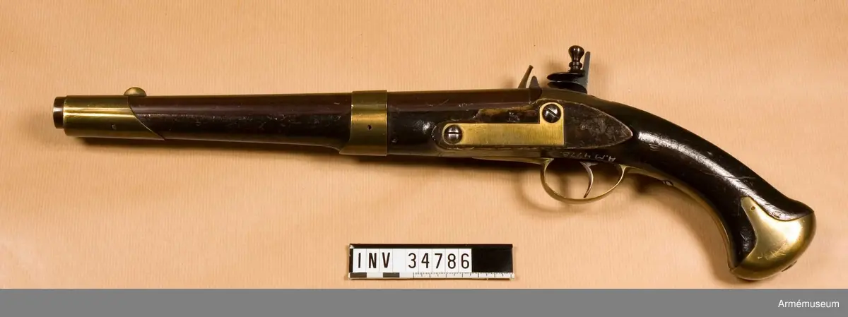 Pistol med flintlås.
Pipan är brungjord. Låset är blånerat. Pistolen har mässingsbeslag utom ryggbeslaget på kolven, vilket är av järn. På pipans kammarstycke finns en stämpel "Helvig inv.t" Kolven är märkt "I S", på vänster sida ovanför sidblecket.