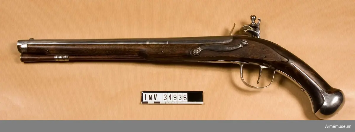 Grupp E III c.
Med flintlås.
Pistolen liknar AM 34859. Vapnets metalldelar är hårt polerade på lumptrissa. På pipans översida finns den krönta rosen, den Örebro-stämpel, vilken ser ut som ett krönt, dubbelt C, och en stämpel med bokstaven S. På vänstra sidan är en obetydlig stämpel, siffran 8 och en stämpel med N I inslagna. Framändan av låsets studel är avrundad och når ej pannstjärten. På låsbleckets utsida finns en stämpel med M. På stämpelns överkant finns en figur, som sannolikt skall föreställa en krona. Den på stockens översida kring svansskruvsstjärten liggande förhöjningen avslutas här av en smal spets. Bakom svansskruvsstjärten är E K inslaget. På stockens vänstra sida bakom sidblecket finns siffran 6 och på kolven vänstra sida vid kolvkappans kant är siffran 8 inslagen. Stocken är tjockt bestruken med dålig fernissa. Kolvkappan är 6 cm lång och 4,9 cm bred. Skenorna är långa och den högra slutar 1,2 cm bakom låsets bakspets. På vänstra sidan sitter en stämpel med E S. Sidblecket är S-formigt samt kullrigt och av järn. Det syns taget från en pistol m/1731. Laddstocken är av trä och på tjockänden skodd med en mässingsplåtskiva. Den sitter orubbligt fast i rännan. 

Pistolen kallas i Modellsalens reversal för m/1704. Mellan 1879 och 1933 har den tillsammans med en del andra pistoler, se AM 34934, 9912, 11920-11930, varit uppsatt som dekoration i II:2. Om det över huvud taget är fråga om en pistol m/1704 är tämligen tvivelaktigt. Vapnet kan mycket väl vara en av delar från diverse äldre pistoler sammansatt reparationsmodell.