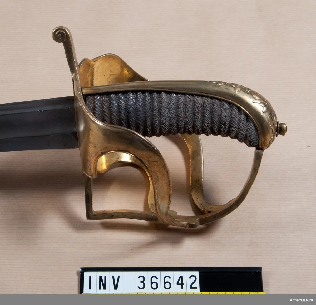 Sabeln är lik modellsabeln AM 36629, men avviker i frågan om fästets ornering. Den på kappan kring nitknappen anbringade ciselerade kransen är här större och går ned på ryggbeslaget och den på yttersidans parerplåt anbringade skölden med tre kronor är här större, ej krökt, nära nog cirkelrund och de sillerade palm- och lagerkvistar, som omger denna sköld, är här vida större och går in på ytterspängerna. Egendomligt nog finns såväl i Livrustkammaren som i ingenjör Orres samling sablar av denna typ, som på klingan har svenska riksvapnet med hessiska hjärtvapnet.