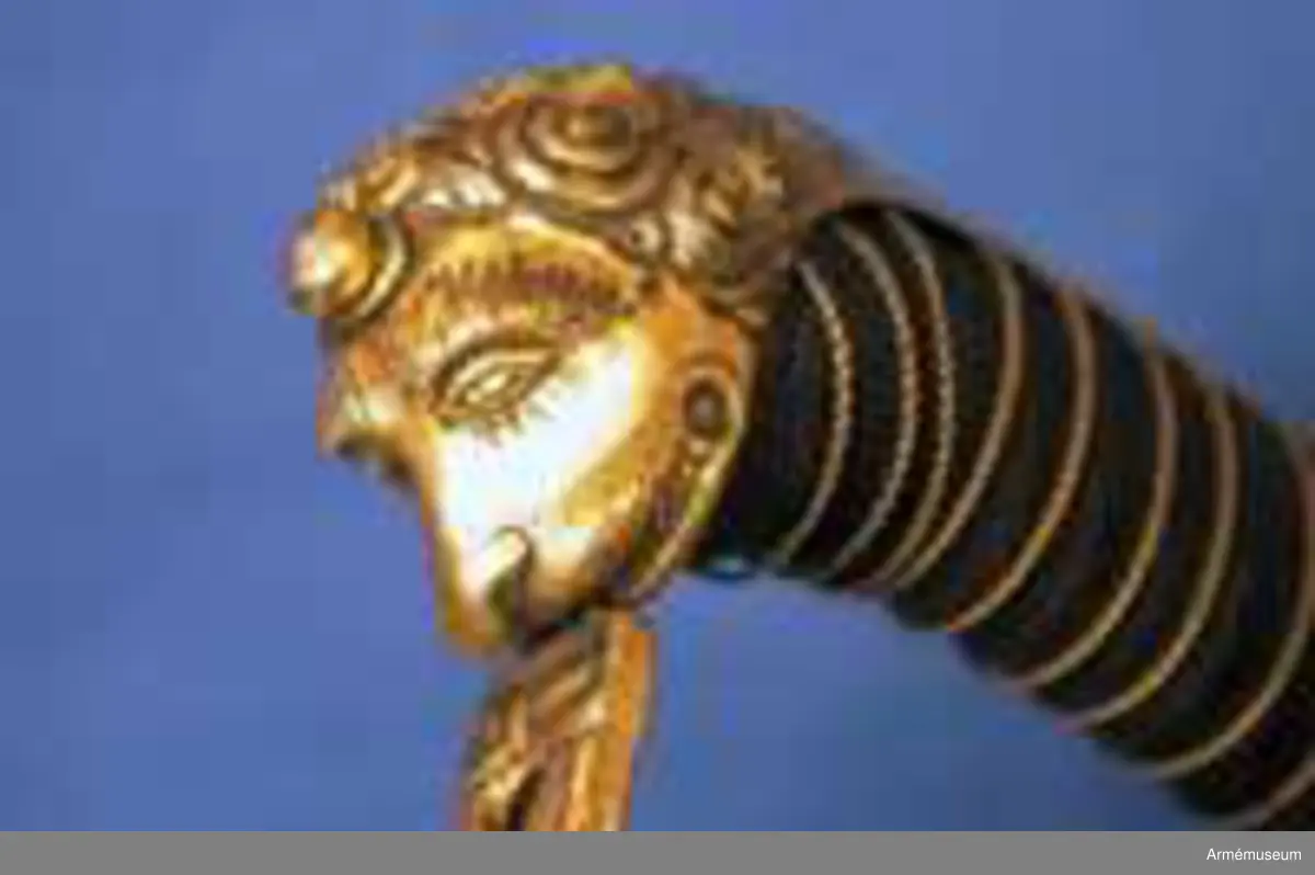 Klingans bredd upptill: 30 mm.Klingan är krökt, skålslipad och har nedtill en svart  betonad, tveegad klack. Fästet är av förgylld mässing. Kaveln är klädd med svart skinn en spiralräffla 16 varv. I bottnen på denna räffla är en av två parter hopsnodd, tunn mässingtråd anbringad. Baktill har kaveln ryggbeslag, som upptill övergår i en kappa, vilken är ciselerad i form av ett lejonhuvud och på vilken sitter en liten nitknapp. Parerstången är en rak och har fyrkantigt tvärsnitt samt av- slutas baktill av en nedböjd, på sidorna med ett spiralornament prydd knapp. Från parerstången främre ände utgår handbygeln i rät vinkel. Handbygeln är längs mitten litet försänkt och har längs var och en av framsidans kanter en ingraverad rand. Litet framför kappan genombrytes den av ett runt hål, och kring detta hål finns ciselerade ornament vilka bilda en stiliserad krans. På yttersidan finnes en uppåtböjd, delvis genombruten parerplåt, som är prydd med krönt sköld med tre kronor, vilken sköld omgives av ett par palmkvistar, allt i ciselerat arbete. Från parerplåtens spets utgår en delvis genombruten och sparsamt med ciselerade ornament prydd S-formig spång, som går till hand- bygelns övre del. På innersidan finns en liknande men mindre, ej genombruten och ej ciselerad parerplåt, från vars spets en S-formig spång går till handbygeln, vilken den träffar något längre ned än ytter- spången. Innerspången prydes längs kanterna av ingraverad rand.