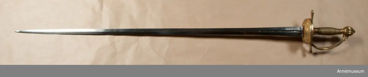 Klingans bredd upptill är 30 mm. Parerstångens längd är 145  mm. Klingan är tveeggad med flata åsar samt har på ömse sidor en blodrand, vid vars slut klingan prydes av ett ornament. Fästet är ett "franskt fäste" av ursprungligen förgylld mässing. Knappen är oval, upp- och nedtill tillplattad och på sidorna prydd med räfflor. Nitknappen är låg, runt sidorna krusad, nedåt instrypt och försedd med en stor, rund fot. Halsen är instrypt och kring sin nedre kant krusad. En rand eller snarare avsats markerar gränsen mellan knappen och nitknappen samt mellan knappen och halsen, och en sådan går även runt halsens nedre del. Kaveln är spolformig med ovalt tvärsnitt och lindad med tre mässingstrådar, av vilka en är slät, men de båda andra  är sammansnodda av två parter; den ena tråden är höger-, den  andra vänstersnodd. Upp- och nedtill omges kaveln av ett omkring 8 mm brett, med tre ränder prytt band av förgyllt  mässingsbleck. Parerstången har närmast sexkantigt tvärsnitt, blir tjockare mot ändarna och pryds där, i likhet med handbygelns mitt, av sex räfflor. Parerplåten är på mitten prydd med ciselerade ornament, men är i övrigt fint prickig samt genombruten av runda hål.