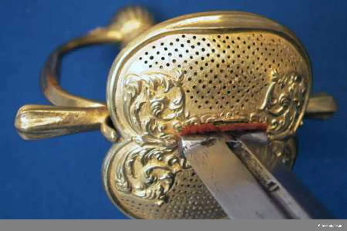 Klingans bredd upptill är 30 mm. Parerstångens längd är 145  mm. Klingan är tveeggad med flata åsar samt har på ömse sidor en blodrand, vid vars slut klingan prydes av ett ornament. Fästet är ett "franskt fäste" av ursprungligen förgylld mässing. Knappen är oval, upp- och nedtill tillplattad och på sidorna prydd med räfflor. Nitknappen är låg, runt sidorna krusad, nedåt instrypt och försedd med en stor, rund fot. Halsen är instrypt och kring sin nedre kant krusad. En rand eller snarare avsats markerar gränsen mellan knappen och nitknappen samt mellan knappen och halsen, och en sådan går även runt halsens nedre del. Kaveln är spolformig med ovalt tvärsnitt och lindad med tre mässingstrådar, av vilka en är slät, men de båda andra  är sammansnodda av två parter; den ena tråden är höger-, den  andra vänstersnodd. Upp- och nedtill omges kaveln av ett omkring 8 mm brett, med tre ränder prytt band av förgyllt  mässingsbleck. Parerstången har närmast sexkantigt tvärsnitt, blir tjockare mot ändarna och pryds där, i likhet med handbygelns mitt, av sex räfflor. Parerplåten är på mitten prydd med ciselerade ornament, men är i övrigt fint prickig samt genombruten av runda hål.
