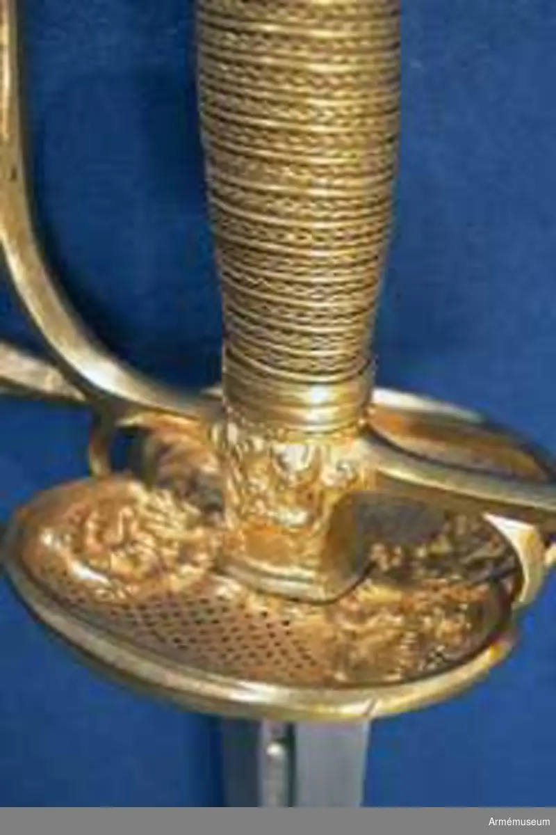 Klingans bredd upptill är 30 mm. Parerstångens längd är 145  mm. Klingan är tveeggad med flata åsar samt har på ömse sidor en blodrand, vid vars slut klingan prydes av ett ornament. Fästet är ett "franskt fäste" av ursprungligen förgylld mässing. Knappen är oval, upp- och nedtill tillplattad och på sidorna prydd med räfflor. Nitknappen är låg, runt sidorna krusad, nedåt instrypt och försedd med en stor, rund fot. Halsen är instrypt och kring sin nedre kant krusad. En rand eller snarare avsats markerar gränsen mellan knappen och nitknappen samt mellan knappen och halsen, och en sådan går även runt halsens nedre del. Kaveln är spolformig med ovalt tvärsnitt och lindad med tre mässingstrådar, av vilka en är slät, men de båda andra  är sammansnodda av två parter; den ena tråden är höger-, den  andra vänstersnodd. Upp- och nedtill omges kaveln av ett omkring 8 mm brett, med tre ränder prytt band av förgyllt  mässingsbleck. Parerstången har närmast sexkantigt tvärsnitt, blir tjockare mot ändarna och pryds där, i likhet med handbygelns mitt, av sex räfflor. Parerplåten är på mitten prydd med ciselerade ornament, men är i övrigt fint prickig samt genombruten av runda hål.