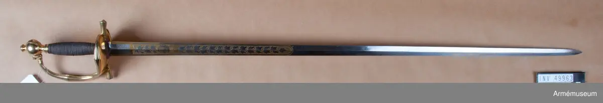 Grupp D II.
Klingan är tveeggad med ryggar. På vardera sidan är den på en längd av omkring 32 cm prydd med blanka, etsade ornament på förgylld botten, däribland på yttersidan Karl XIV Johans namnchiffer och en ranka med lagerlöv, på insidan med tre kronor under kunglig krona samt en ranka med eklöv och ollon. Fästet är av förgylld mässing och av karolinsk kavallerityp. Knappen har formen av ett tillplattat klot samt har fram och bak en rygg markerad av en längs kanterna upphöjd rand. Nitknappen är rätt hög, svagt fasonerad och med ganska stor fot. Nedtill  fortsätts knappen av en på mitten instrypt hals. Runt halsens nedre del går en rand. Gränsen mellan hals och knapp samt mellan knapp och nitknapp är tydligt markerad. Kaveln omges upp- och nedtill av ett ringliknande, omkring 5 mm brett beslag av förgyllt mässingsbleck. Längs varje kant pryds dessa beslag av en ingraverad rand. I övrigt är kaveln lindad  med en tunn, av två parter hopsnodd försilvrad koppartråd. Parerstången vidgas rätt kraftigt mot de i trepass avslutade ändarna samt har ovalt tvärsnitt. Längs dessa övre och undre, främre och bakre kanter går en upphöjd rand. Parerplåten är hjärtformig. Dess förhöjda kanter är på mitten vidgade och har på samma ställe en kantig utbuktning på den mot plåten motsatta sidan. Handbygeln vidgas rätt kraftigt på mitten och har ovalt tvärsnitt. Dess övre ände är medelst en skruv fäst vid knappen. Längs över- och undersidan på de förhöjda kanterna samt längs handbygelns främre och bakre kant löper en upphöjd, smal rand. På översidan av parerplåtens yttre hälft är de ciselerade bokstäverna F J O (Frans Josef Oskar) fastnitade och på samma sida av den inre hälften är en kronprinskrona i liknande arbete fäst.