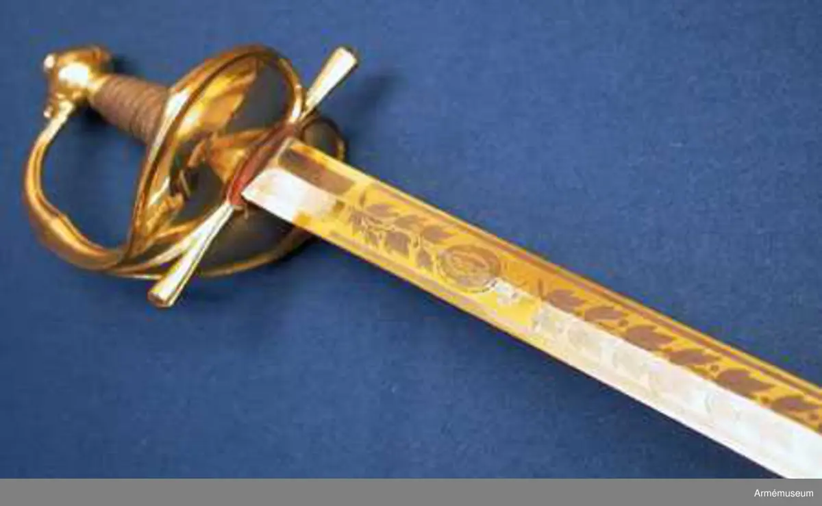 Grupp D II.
Klingan är tveeggad med ryggar. På vardera sidan är den på en längd av omkring 32 cm prydd med blanka, etsade ornament på förgylld botten, däribland på yttersidan Karl XIV Johans namnchiffer och en ranka med lagerlöv, på insidan med tre kronor under kunglig krona samt en ranka med eklöv och ollon. Fästet är av förgylld mässing och av karolinsk kavallerityp. Knappen har formen av ett tillplattat klot samt har fram och bak en rygg markerad av en längs kanterna upphöjd rand. Nitknappen är rätt hög, svagt fasonerad och med ganska stor fot. Nedtill  fortsätts knappen av en på mitten instrypt hals. Runt halsens nedre del går en rand. Gränsen mellan hals och knapp samt mellan knapp och nitknapp är tydligt markerad. Kaveln omges upp- och nedtill av ett ringliknande, omkring 5 mm brett beslag av förgyllt mässingsbleck. Längs varje kant pryds dessa beslag av en ingraverad rand. I övrigt är kaveln lindad  med en tunn, av två parter hopsnodd försilvrad koppartråd. Parerstången vidgas rätt kraftigt mot de i trepass avslutade ändarna samt har ovalt tvärsnitt. Längs dessa övre och undre, främre och bakre kanter går en upphöjd rand. Parerplåten är hjärtformig. Dess förhöjda kanter är på mitten vidgade och har på samma ställe en kantig utbuktning på den mot plåten motsatta sidan. Handbygeln vidgas rätt kraftigt på mitten och har ovalt tvärsnitt. Dess övre ände är medelst en skruv fäst vid knappen. Längs över- och undersidan på de förhöjda kanterna samt längs handbygelns främre och bakre kant löper en upphöjd, smal rand. På översidan av parerplåtens yttre hälft är de ciselerade bokstäverna F J O (Frans Josef Oskar) fastnitade och på samma sida av den inre hälften är en kronprinskrona i liknande arbete fäst.