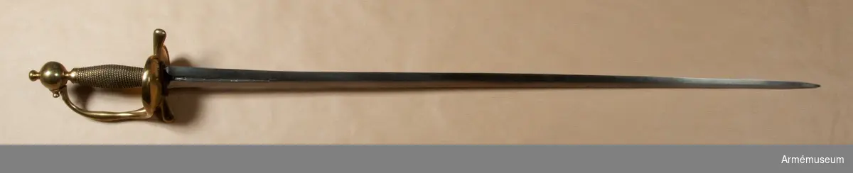 Klingan är tveeggad. Upptill på bägge sidor har den en omkring 140 mm lång blodrand. På yttersidan sitter dessutom en P-stämpel. Vid varje blodrands nedre ände finns ett delvis bortslipat, av prickar bestående ornament. Klingan är starkt avslipad, så att åsarna nedanför blodrandens slut nära nog förvandlats till ryggar. Fästet är av mässing och av drabanttyp. Knappen har formen av ett hoptryckt klot samt har rygg på fram- och baksidan. Knappens diameter är i sidled 37,5 mm, men över ryggarna 40,5 mm. Höjden är 33 mm. Upptill har knappen en stor nitknapp, som är instrypt. Nitknappens höjd är 16 mm, och diametern är 16 mm. Den har en spetsoval fot, som är 22 mm lång och 17 mm bred. Halsen är instrypt och 11 mm hög. Gränsen mellan nitknappen och knappen samt mellan knappen och halsen markeras genom en rand eller avsats. En dylik går även kring halsens nedre del. Knappen är rätt illa gjuten. Kaveln är spolformig, har fram och bak en flat rand, men sidorna är kullriga. Den har upp- och nedtill ett omkring 8 mm brett ringliknande beslag av mässingsbleck, varje beslag är prytt med två ränder samt är i övrigt lindat med två mässingstrådar, en grövre och en finare, vardera hopsnodd av två parter. Den ena tråden är höger-, den andra vänstersnodd. Parerstångens armar har spetsovalt tvärsnitt, är nedåtböjda samt blir mot de lindrigt avrundade ändarna tjockare och betydligt bredare. Den största tjockleken är för den främre armen 18,5 mm och för den bakre 18 mm. Avståndet mellan den främre eggen och  parerstångens framände är 54,5 mm. Mellan den bakre eggen och  bakänden är avståndet också 54,5 mm. Avståndet mellan klingans mitt och parerplåtens ytterkant är 52 mm, men mellan klingans  mitt och innerkanten 46 mm. Handbygeln är tjockast och bredast ungefär på mitten. Den har spetsovalt tvärsnitt och dess övre ände är fäst med en skruv vid knappen. På yttersidan av parerstångens främre arm finns en stämpel med bokstäver, sannolikt N. S.