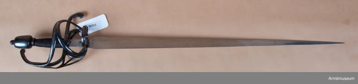 Den tveeggade klingan är upptill rätt bred samt avsmalnar långsamt och likformigt mot udden så att den får formen av en långdragen triangel. På vardera flatsidan har klingan längsgående rygg, och upptill en cirka 65 mm lång ansats, som har plana flatsidor och svagt kullriga eggsidor. Vid klingbasen är ansatsen 28 mm men vid fästet 19 mm bred. Längs var och en av ansatsens långkanter går på flatsidorna en ingraverad rand. På var och en av ansatsens flatsidor finns en krönt stämpel med bokstaven S över bokstaven T, samt på innersidan dessutom bokstäverna H Z under en krona, vilket lär betyda Hauptzeughaus. Fästet är av svärtat järn. Knappen har närmast formen av en långdragen, stympad kon med kullrig översida och med rygg längs var eggsida, så att den får spetsovalt tvärsnitt.  Nitknappen är rätt hög och avskiljes genom en horisontal fals  från knappen. Knappens hals är kort och kullrig samt  avskiljes även den genom en horisontal fals från knappen. På yttersidan av knapphalsens underkant finns fyra inhuggna streck.

Träkaveln är närmast spolformig, men betydligt bredare vid korset än vid knappen. Flatsidorna är kullriga, men längs vardera eggsidan går en försänkt rand. Nedtill har kaveln krans av snodd järntråd, men den övre kransen är förkommen. Kavellindningen består av en rätt grov, överspunnen järntråd samt av en höger- och en vänstersnodd järntråd, vardera hoptvinnad av två parter. Parerstången har spetsovalt tvärsnitt samt vid korset på var sida en trekantig, nedåtvänd flik. Baktill är parerstången nedböjd och avslutas med en skivformig utsvällning, som är svängd litet åt yttersidan. Framtill övergår parerstången bågformigt i handbygeln, vilken upptill avslutas med en flat skiva, vars kant står några millimeter framför knappen. Från korset utgår vid var och en av ansatsens eggsidor en stor,  nedåtriktad fingerhake. De båda fingerhakarnas nedre ändar förenas på yttersidan med en horisontal bygel. På samma sida utgår även en från fingerhakarnas nedre ändar en snett uppåtriktad, i ca 45 graders vinkel ställd stor parerbygel, vars övre kant står i jämnhöjd med kavelns nedre del. Från  den hösta punkten på denna bygel går en spång till handbygelns mitt. På innersidan går en nedtill tregrenigt S-formig gaffelspång från handbygelns mitt till fingerhakarnas nedre ändar. Gaffelspångens olika delar har cirkelrunt tvärsnitt, men yttersidans byglar och spång har kullrig utsida och flat insida.