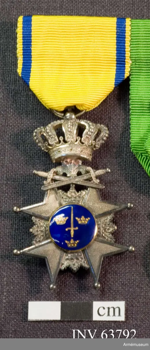 Grupp M II.
Svärdsmannatecken med band tilldelat styckjunkaren Georg Wilhelm Wessman.  Ett snedställt johannitkors av silver. Åtta uddar, var och en slutande i en kula. Mellan korsarmarna öppna kronor. På åtsidan har tecknet en blå, emaljerad glob i korstets mitt med ett stolpvis ställt svärd och tre öppna kronor ställda två och en. Mellan korsets övre vänstra udd och övre högra störtande svärd. Frånsidans mittglob är av silver med ett stolpvis ställt svärd omlagt med två kvistar ovanför "PRO PATRIA". Tecknet hänger i en kunglig krona. Medaljband av ett 35 mm brett sidenripsband - gult med mörkblå kantrand. 