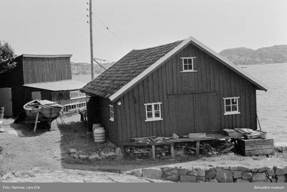 Motivbeskrivning: "F.d varv i Skredsvik, längst fram i bild båtbyggarverkstaden. Till vänster virkesmagasinuppförd i slutet av 1940-talet, den låga tillbyggnaden vid virkesmagasinet (utrymme för bl.a kutterhyvel) tillkom i slutet av 1960-talet. Mellan virkesmagasin och båtbyggarverkstaden syns en bohusjulle byggd år 1951 av Karl Johansson (se Bb 17:21)."
Datum: 19800717
Riktning: Sö