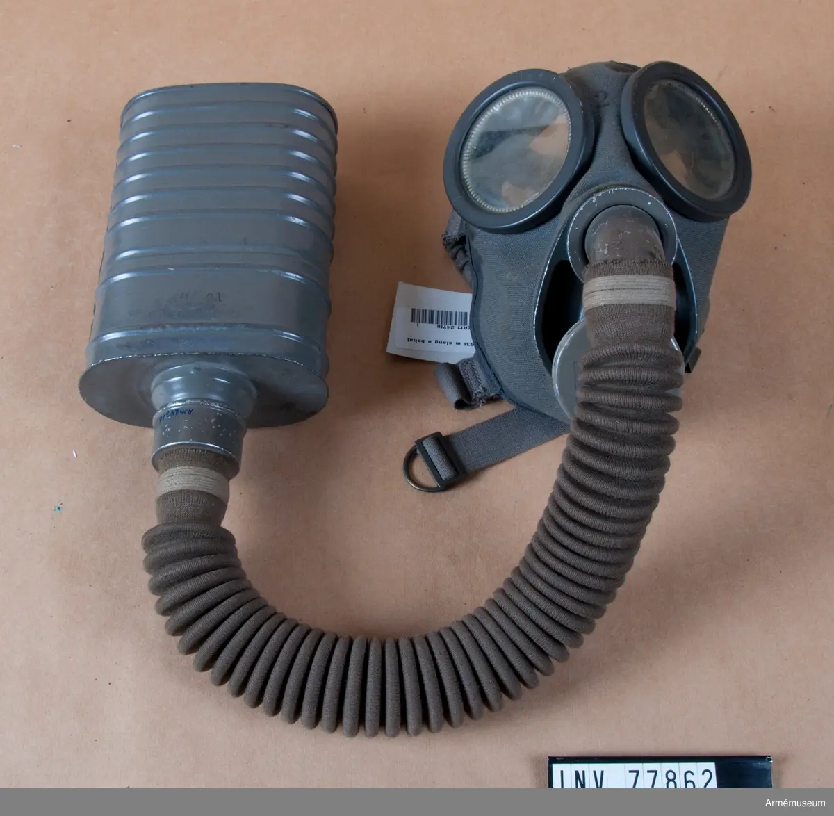 Grupp J.
Gasmask m/1931. Komplett med väska.
Består av ett ansiktsskydd m/1931, en ask för imskivor i reserv, en ask för ventilhus i reserv, en behållare m/1931, en slang, två ventilhus samt en väska m/1931.