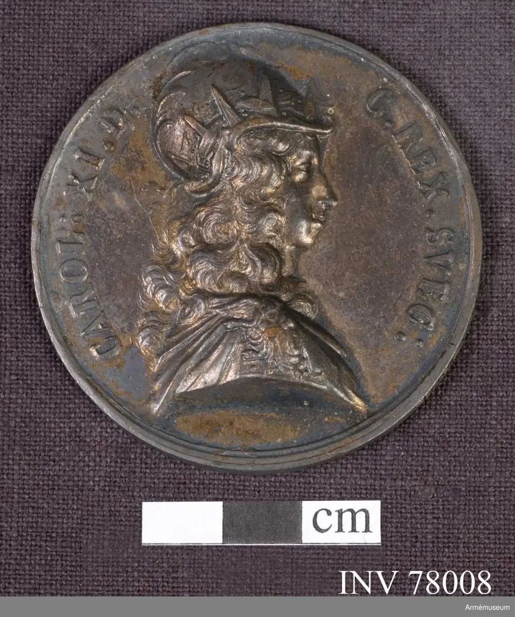 Grupp: M. 
Åtsidan: CAROL. XI. D G. REX. SVEC: Bröstbild åt höger, i harnesk med ett uppvänt ansikte på övra delen, samt harnesk med ett högt Medusahuvud på axeln och mantelveck - Under armen B.

Frånsidan: FACILE RVMPITVR. Ett blottat svärd svävar horisontelt över den sk gordiska knuten, ett av tåg konstigt hopknutet klot, som ligger på ett runt altare. Vid sidorna av knuten: NODVS. GORDI. I bakgrunden ses de stridande härarna, den danska flyende. Överst ett strålande JHVH (med hebreiska tecken). I avskärningen: SCANIA. IV. DEC. M.DC. LXXVI. på två rader.