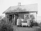 Troligen födelsedagsfirande. Gruppen porträtterad framför bostadshuset vid ett bord fullt av blombuketter i vaser. 
Trea från vänster: Anna på Rultane (mor till Artur). Damen i vit schal är Augusta Forsberg. Bakom henne står Artur Pettersson.