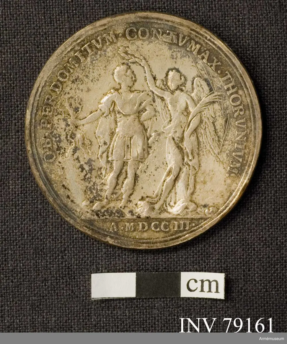 Grupp: M. 
Åtsidan: CAROLVS XII D G REX SVECIAE. Bröstbild åt höger, i slätt harnesk och släta mantelveck vikta över axeln, halsen bar med en veckad remsa över kanten av harnesket - Nedanför AC. 

Frånsidan: OB. PERDOMITVM CONTVMAX THORVNIVM. Segergudinnan, med palmqvist i venstra handen, sätter en lagerkrans på konungen, som står med åskvigg i sin hand - I avskärningen: MDCC III. 

Medaljen präglad av A. Karlsten.