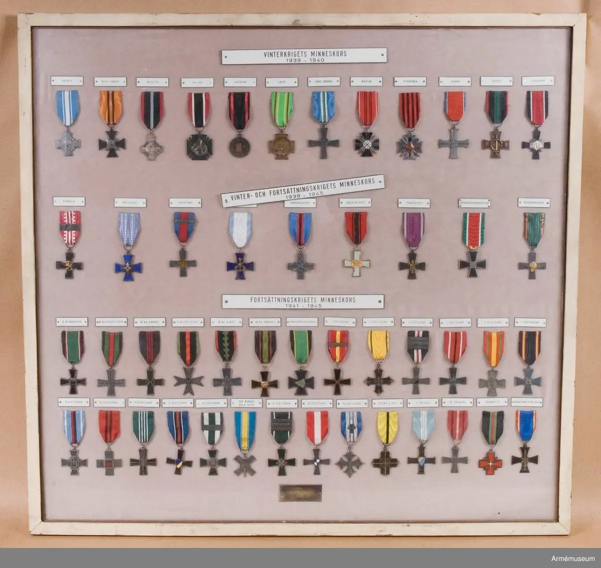 Grupp M:II.
48 stycken, monterade med band på tavla inom glas och ram.
Vinterkrigets minneskors 1939-1940: 1. Kaimne 2. Keski-Kannas 3.Koivisto 4.Kollaa 5.Laatokha 6.Lappi 7.Länsi-Kannas 8.Muolaa 9.Pitkäranta 10.Summa 11.Taipale 12.Tolvajawi. Vinter och fortsättningskrigets minneskors 1939-1945: 1.Päärnaja 2.Kotijonhot 3.Hmavoimat 4.Laivaisto 5.Rannikkojoukot 7.Pioneeiisti 8.Sotarauttatiemuodostelmat 9.Rajajääkärijonkot. Fortsättningskrigets minneskors 1941-1945: 1.II Ak-Maselkä  2.IIIAK-Pohjois-Viena 3.IV AK-Kannas 4.V AK-Itä-Syväri 5.VI AK-Annus 6.VII AK-Ääninen 7.Pansardivisioona 8.1.Divisioona 9.2.Divisioona 10.4.Divisioona 11.5.Divisioona 12.6.Divisioona 13.7.Divisioona 14.8.Divisioona 15.10Divisioona 16.11.Divisioona 17.12.Divisioona 18.14.Divisioona 19 Itä-Kannas(15D-19.Pr) 20.17.Divisioona 21.18.Divisioona 22.19.Divisioona 23.Ryhmä D-Ro Pr 24.3.Prikaati 25.15.Prikaati 26.Prikaati K 27.Jatkosodan lapin risti Tillverkad:.Monteringen utförd av Krigsinvalidernas Brödraförbund R.Y.