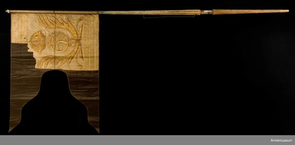 Dragonfana av vit taft med Christian 5's krönta monogram inom korsade palmkvistar. Allt målat i guld. En längre devis på tyska skriven i guldfärg ovan och under monogrammet.