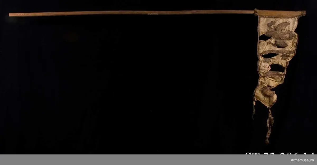 Duk av vit sidentaft och strumpa av rött linne försedd med frans vid öppningarna. Motivet målat i guld- och silver samt rött och grönt bestående av en krönt örn, måne, sol och stjärnor, På duken en pappersetikett som anger att den tagits i slaget vid Saladen 1703.