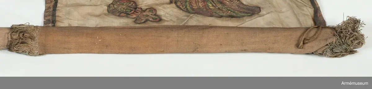 Duk av vit sidentaft och strumpa av rött linne försedd med frans vid öppningarna. Motivet målat i guld- och silver samt rött och grönt bestående av en krönt örn, måne, sol och stjärnor, På duken en pappersetikett som anger att den tagits i slaget vid Saladen 1703.