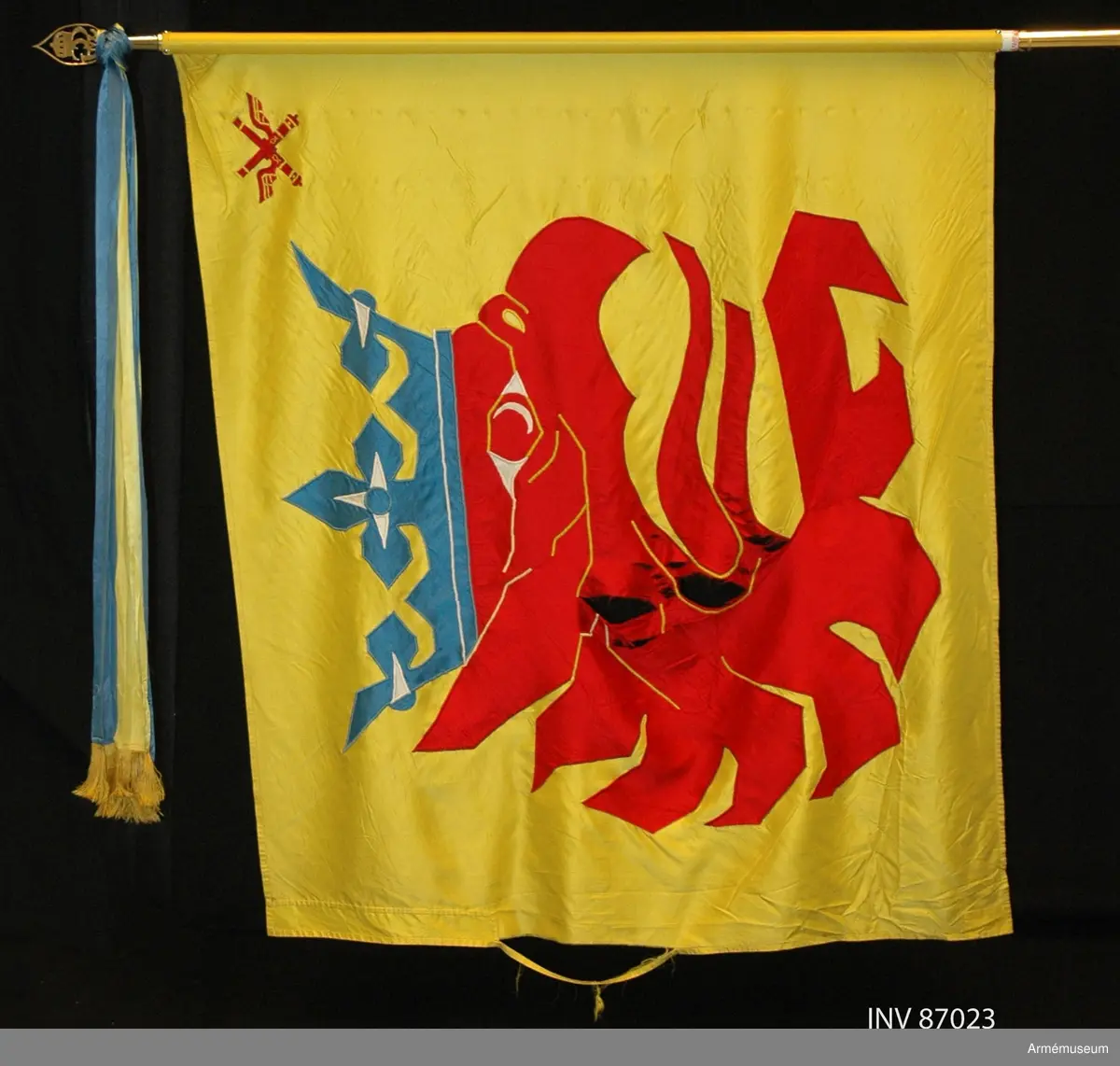 Duk av sidenkypert med landskapet Skånes vapenbild: ett med öppen blå krona krönt avslitet rött griphuvud. I övre inre hörnet två korslagda bevingade röda eldrör av äldre modell. Detta är ett traditionsarv från Skånska luftvärnskåren, Lv4.

Motivet är huvudsakligen utfört i maskinbroderi och intarsia. Vissa detaljer är handbroderade såsom hörnmotivet, näsborren, en del av ögat samt de utskjutande delarna på ömse sidor om kronan. Duken är maskinfållad med sick-sack och raksöm. Triangelformade förstärkningar i övre och nedre stångsidan.

Vitmålad, delbar fanstång. Duken fäst med släta tennlickor. Doppsko av guldfärgad plast, troligen ej ursprunglig. Spets med Carl XVI Gustafs monogram. På holket graverat: "Södra skånska regementet och Södra skånska brigaden 1998".
 
KT 2012-03-06