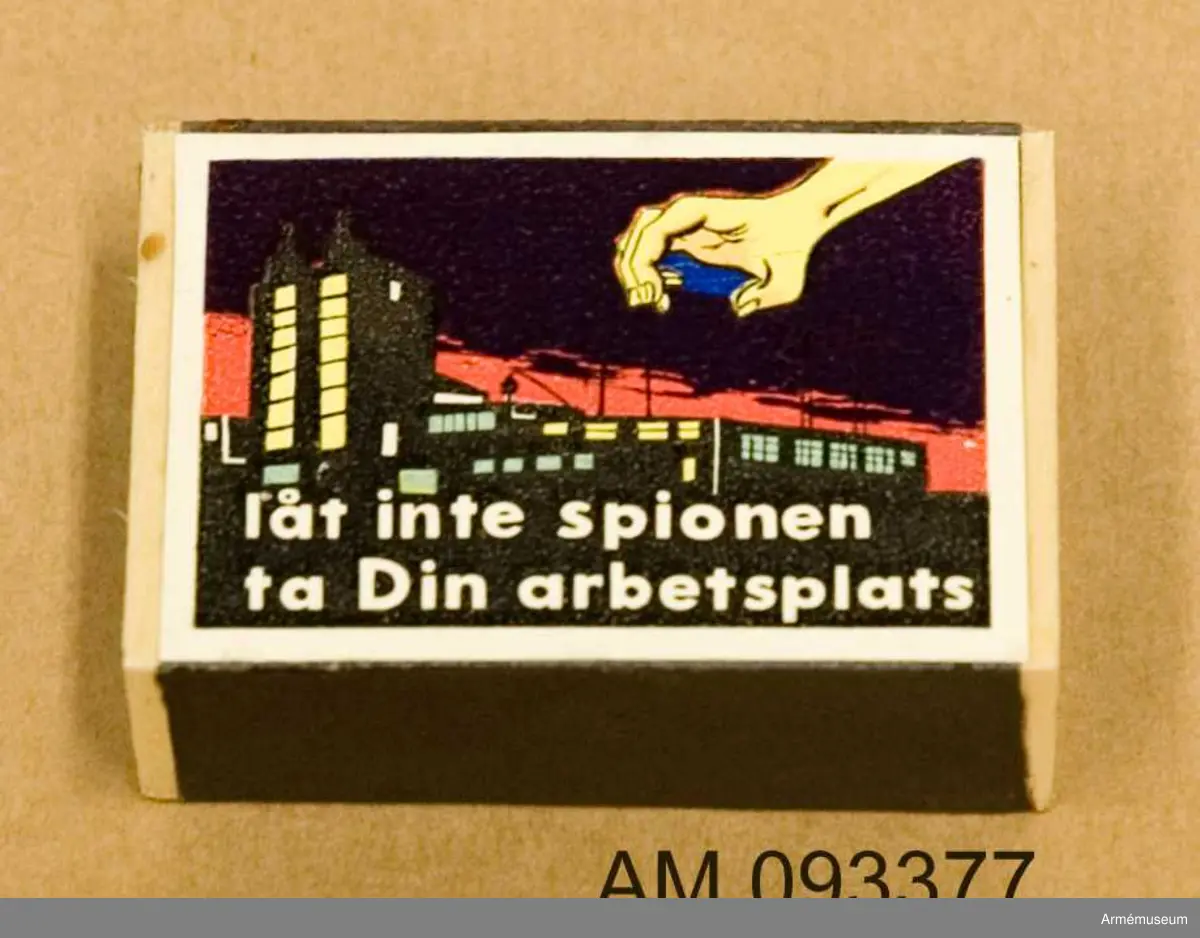 Tändsticksask med tändstickor. På ena sidan motivet Solstickan och på andra sidan ett motiv som illustrerar hur en spionhand sträcker sig över en husbyggnad nattetid. 
