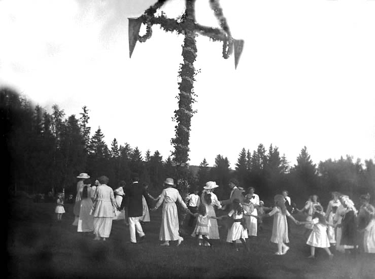 Män, kvinnor och barn dansar runt en midsommarstång