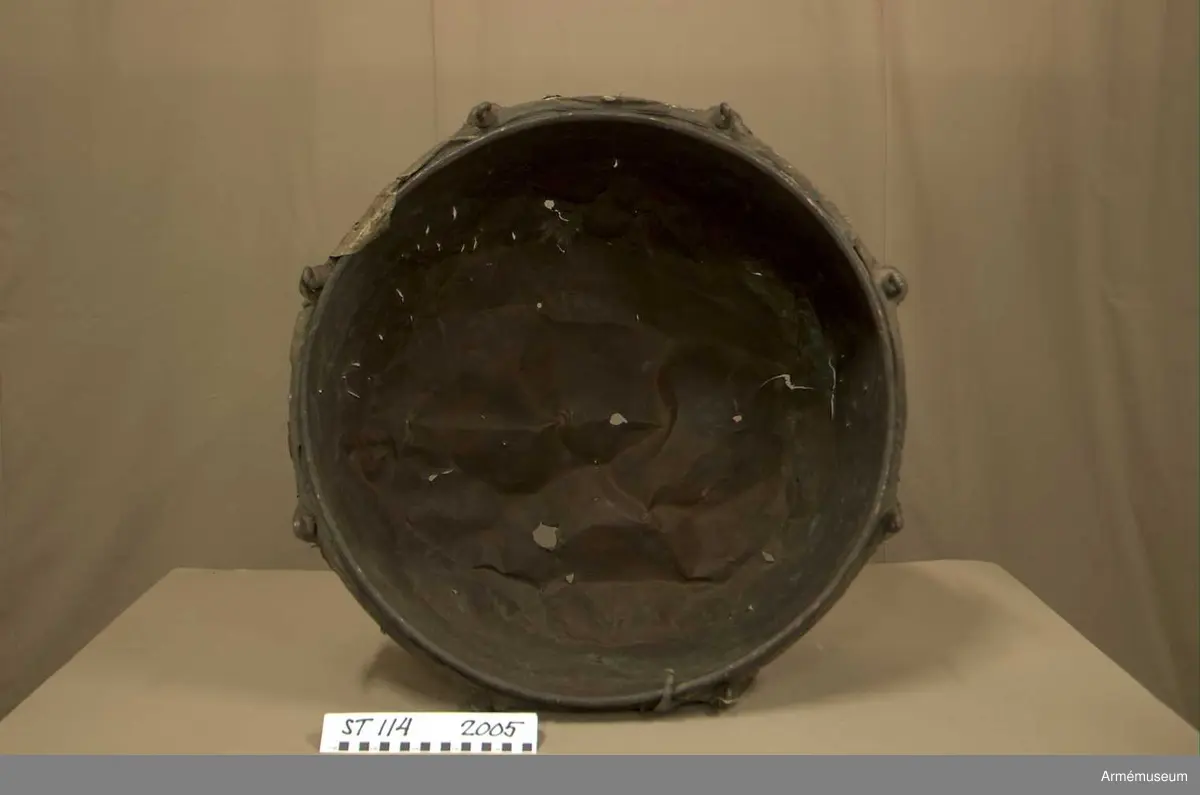 Tillstånd 2005:
Kittel: kraftigt bucklig och sprucken på flera ställen. En mängd stickmärken i storlek 1 cm. - 4 cm. Fot: saknas. Spännskinn: saknas, förutom en liten flik - hängandes över kanten in i pukan - likaså är skinnet lämnat längsmed kittelkanten fastsytt genom ett smalt läderband. Spännring: rostig. Spännskruv: 8 st. Skruvfästen: 8 st. Bärrem: saknas.