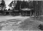 Paviljonger med veranda på Fristad hed, Älvsborgs regementes, I 15, övningsområde. Soldat på cykel och flera män passerar utanför. I bildens nedre högra hörn går en hund.