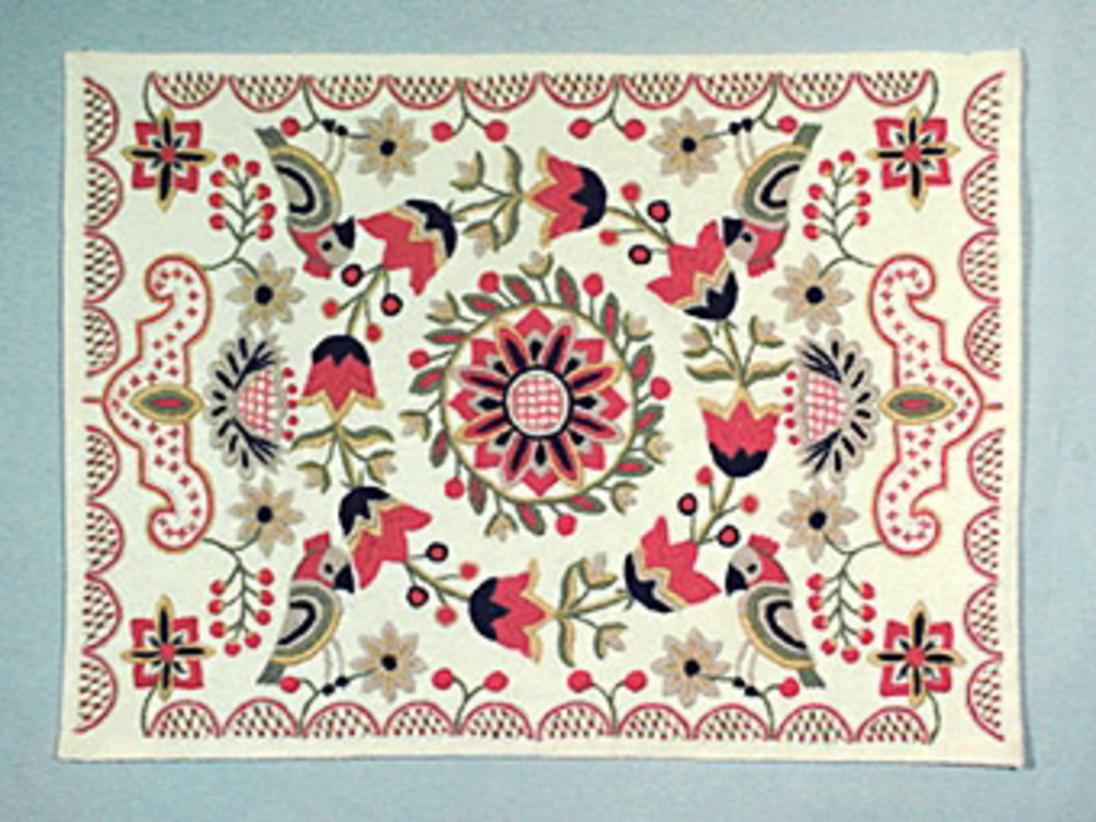 Två stycken bonader broderade på ljust ylletyg 590 X 410 mm på mörkt naturvit, dovare färgskala än 575 X 420 mm. I centrum blomma, blad- och småblomskrans runt, sedan tulpankrans. Bågar i kanten, fyllda med bottensöm. Två papegojor på varje långsida, urna med blommor på varje kortsida. 
Den i ljusare skala, fodrad med halvlinnetyg, sytråd kvar efter upphängningsanordning. Originalversion som åkdyna. Omarbetad av Maja Lundbäck, dåvarande direktris för Hemslöjdsförbundet för Sverige, för Kristianstad Hemslöjds räkning. Se boken "Hemslöjdens handarbeten", (Stockholm 1944), sid 19.