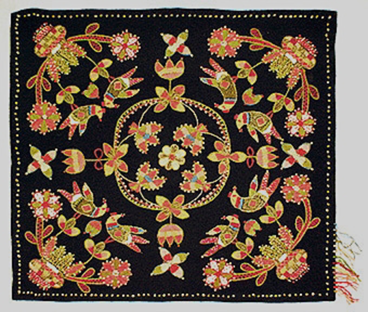 Fyrkantigt svart ylletyg, broderat med yllebroderi i entrådiga (2 st) och tvåtrådiga ullgarner och lingarner. Garnprover fästade vid ena kanten. Motiv med liten blomma i centrum, ringad av blommor och en krans varifrån blommor hänger ut en mot varje kant. I varje hörn en urna med flertalet blommor varpå parvis ställda fåglar sitter. Ram med knutsöm 11 mm från kanten. Fållad.Efter original som är ett jynne och finns på Länsmuseet i Kristianstad.
Se också broderiprov KHL.A6:53.
