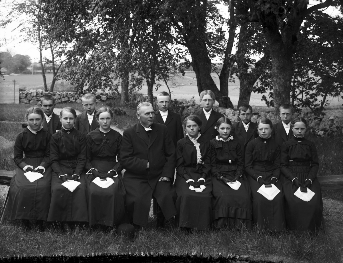 Konfirmandgrupp, sannolikt vid Vallby kyrka, Uppland. I mitten sannolikt kyrkoherde Gustaf Thegerström (1853-1937).