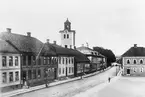 Östra Storgatan i Jönköping österut. Till höger ligger Hovrättstorget. I ett hus till vänster finns Kongl.Postkontoret och M.Hallbergs bageri. Tornet på Kristine kyrka höjer sig över hustaken.