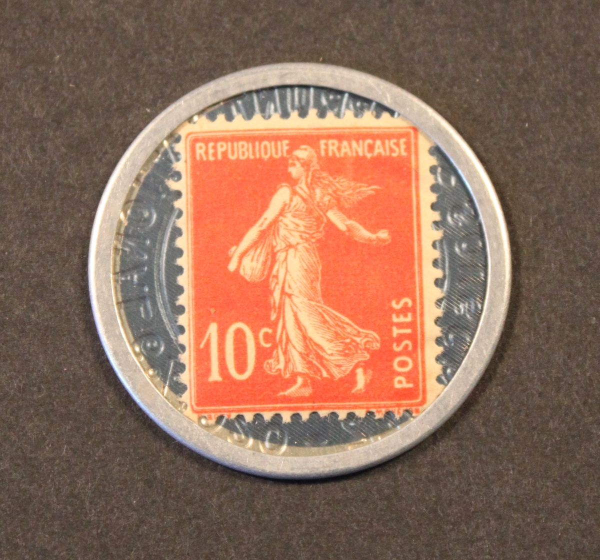 Frimärke 10 centimes i rund hylsa av aluminiumplåt
(liknandeen fickspegel). Framsidan genomskinlig (celluloid över
frimärket).Använt som skiljemynt i Frankrike efter första
världskriget.