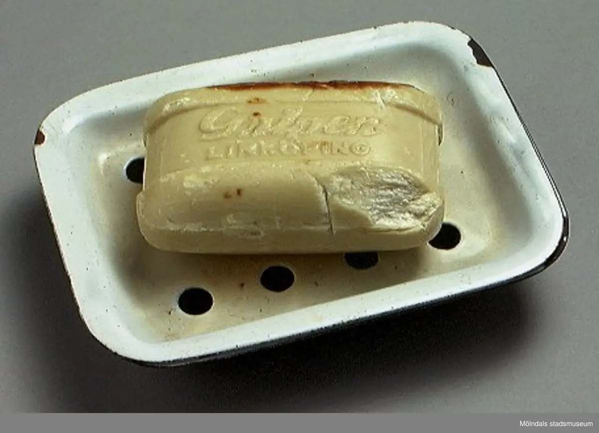 Emaljerad tvålkopp bestående av två delar: vit bricka med hål och ett fat med vit insida och gråblå utsida.
