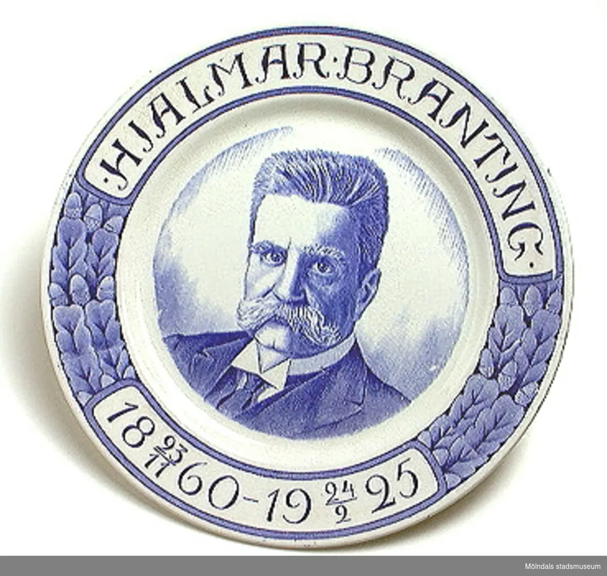 Vit minnestallrik. Blått tryck med texten "Hjalmar Branting 23/11 1860 - 24/2 1925" samt en bild av Branting i mitten av tallriken.