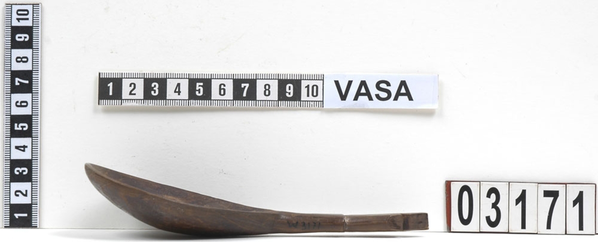 En träsked.
Skeden har ett ovalt skedblad och ett kort skaft. Skaftet är profilerat i tre avsatser. Skaftets ände är formad till en spets. På skeden syns spår av färg.
Skeden är mycket välbevarad, bortsett från en liten spricka som är synlig på baksidan.

Text in English: Wooden spoon with egg-shaped bowl and short, profiled handle ending in a point.
Intact and well preserved except for a small crack on the reverse.