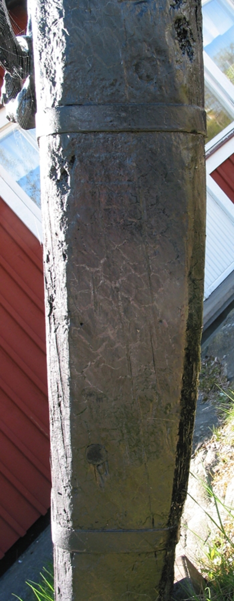 Stockankare. Trästock med fyra järnband samt en skyddskåpa i metall över ändträet på övre delen. Stockens två delar hålls ihop med fyra kilade trädymlingar. Stocken är på vissa partier mycket sliten. Schackel i röringen.