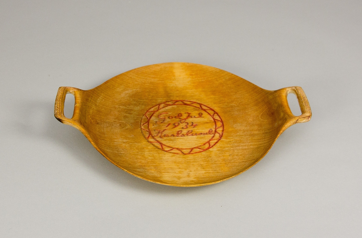 Fat av trä. Runt med två handtag. Svarvat och skuren. Skuren och målad dekor i fatets spegel i form av en julhälsning: "God Jul 1934 Karlslund" i en rund bård med våglinje. Även skuren och målad dekor handtagen.