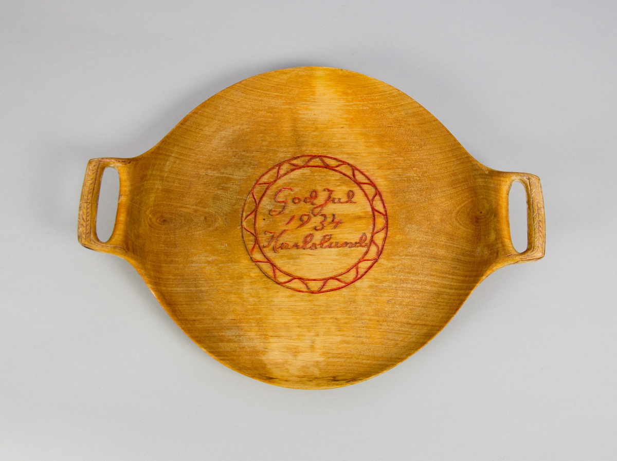 Fat av trä. Runt med två handtag. Svarvat och skuren. Skuren och målad dekor i fatets spegel i form av en julhälsning: "God Jul 1934 Karlslund" i en rund bård med våglinje. Även skuren och målad dekor handtagen.