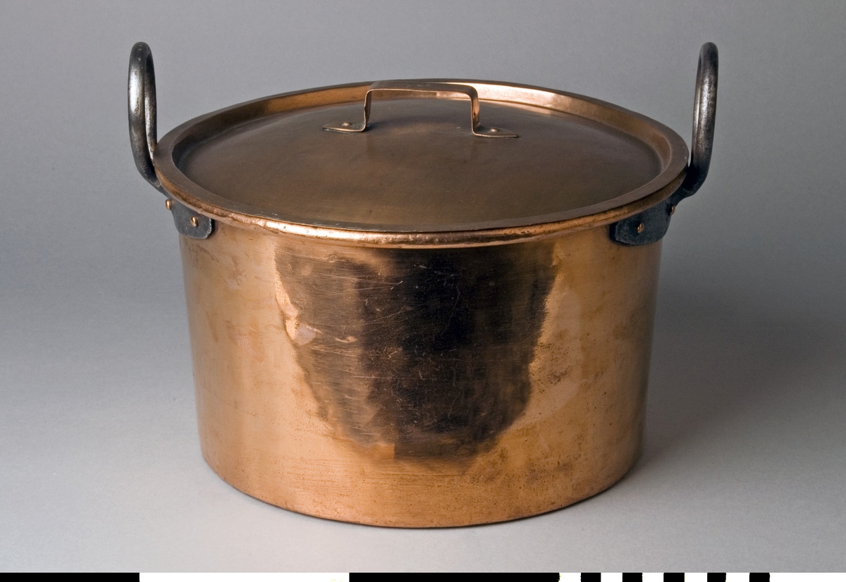 Gryta med lock tillverkad av koppar. Lock med bygelhandtag fäst med två nitar. Fals runt kanten. Märkning på bygeln: C.A.C. Locket är troligen av senare tillverkning. Grytan har en förtent insida. Lätt utåtlutande sidor, 167 mm höga. Överkanten är rullad utåt runt en stödtråd. Runda grepar av grov järntråd med utsmidda avlånga fästen, fyra rullade nitar till varje grep.