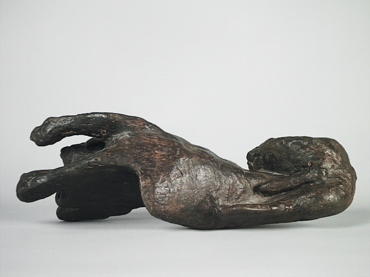 Skulptur av ett litet, liggande lejon med utsträckta framben och hopdragna bakben.
Lejonet är riktat mot vänster, sett från betraktaren. Det snett hållna huvudet återges i det närmaste i en face. Större delen av svansen saknas. Den befintliga delen av svansen avtecknar sig mot lejonets vänstra lår.

Lejonet är endast delvist rundskulpterat. På baksidan, i höjd med huvudet och höger framben, återfinns ett stort, snett urtag som bildar en slät anliggningsyta. Skulpturens framparti är således endast till hälften så tjockt som dess bakparti.
Bakkroppen är kraftigt sliten och skadad. Vänster bakben saknas, liksom större delen av svansen.

Text in English: Sculpture of a small reclining lion with its forelegs extended and its  hind legs tucked beneath its body.
Facing to the observer''s left, the head, held crookedly, is nearly en face. A large part of the tail is missing, and the remainder curves towards the left hind leg.

The lion is only partly three-dimensional. On the rear at the head height and at the right foreleg a large oblique hole forms a flat area for attachement, thus the forepart of the sculpture is thus only half as thick as its rear.
The rear of the body is badly worn and damaged. The left hind leg has been broken off.