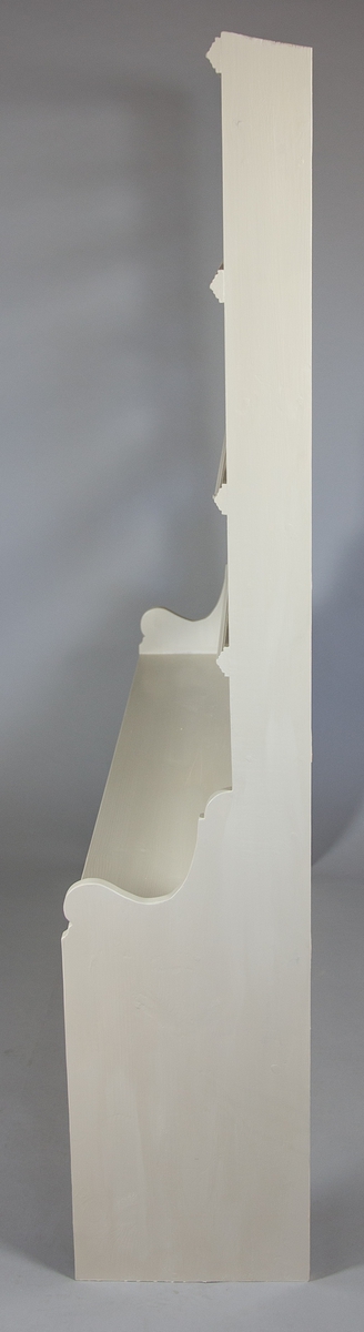 Hylla tillverkad av furu. Profilerade gavlar. Nedtill skiva och upptill fem hyllplan. Varje hyllplan har en profilerad list.