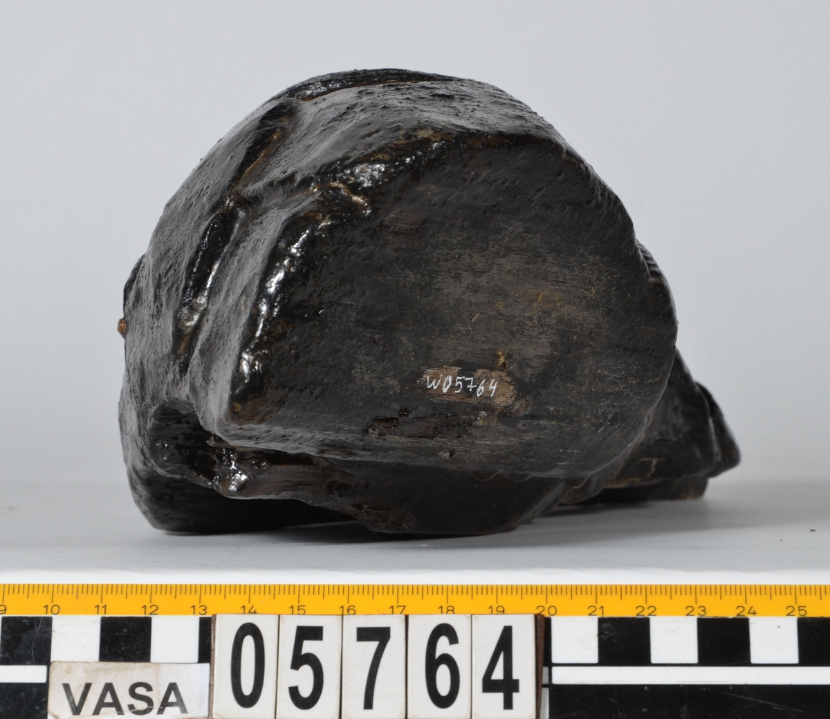 Del av skulptur, nedre del till fiskstjärt. Avsmalnande i ena änden. Rundad framsida med utsnidade fiskfjäll. Baksidan är bruten.